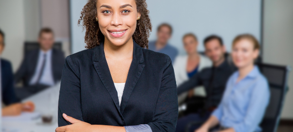 Woman professional looking at the camera with a group of people at a conference table behind her